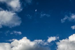 Half moon at a distance on a clear day surrounded by cotton wool like clouds