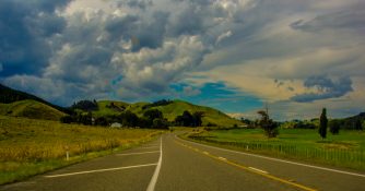 driving past a land lush with green vegetation and a small hill